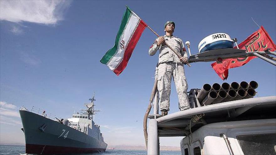 Un soldado de la Armada iraní lleva la bandera nacional en un buque de guerra.