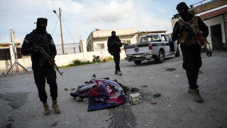 Miembros de las fuerzas del actual gobierno sirio junto a un cadáver en Latakia, 9 de marzo de 2025. (Foto: EFE)