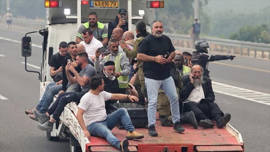 Un grupo de colonos israelíes debajo de un camión escapa de sus hogares por fuego, 30 de abril de 2025.
