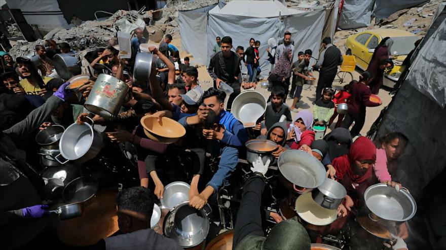 Palestinos hacen fila para recibir comida caliente, distribuida por organizaciones benéficas, mientras continúan el embargo y los ataques israelíes, el 3 de mayo de 2025. (Foto: Anadolu).