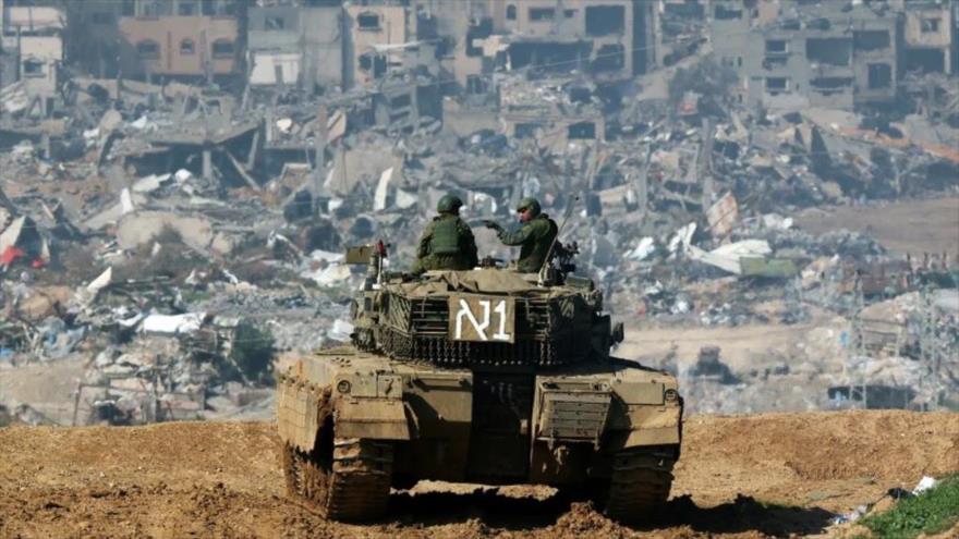 Un tanque israelí avanza hacia Gaza mientras se ven edificios destrozados en el enclave costero palestino al fondo, enero de 2024. (Foto: AFP)