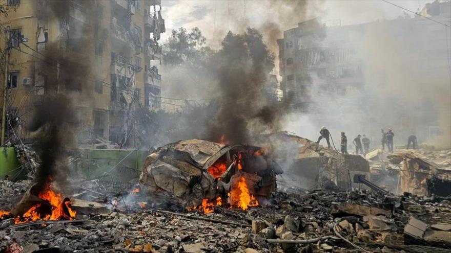 Un bombero rocía agua sobre los escombros mientras la gente se congrega en el lugar de un ataque israelí en el sur de Beirut, capital del Líbano, 28 de maro de 2025. (Foto: AFP)