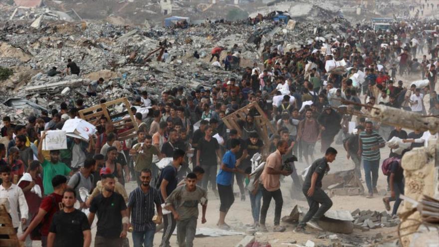 Varias personas cargadas de ayuda caminan por la calle al-Rashid, en el oeste de Yabalia, después de que camiones de ayuda humanitaria entraran en el norte de la Franja de Gaza a través del paso fronterizo de Zikim.
