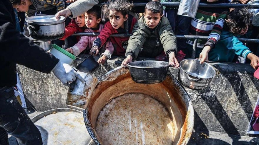 Palestinos se reúnen para recibir comida por una cocina benéfica en la Franja de Gaza.