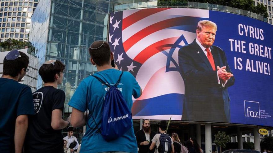 Jóvenes observan un cartel colgado en Tel Aviv, en el que refiriéndose a Trump se lee ‘Ciro el Grande está vivo’, 12 de octubre de 2025.