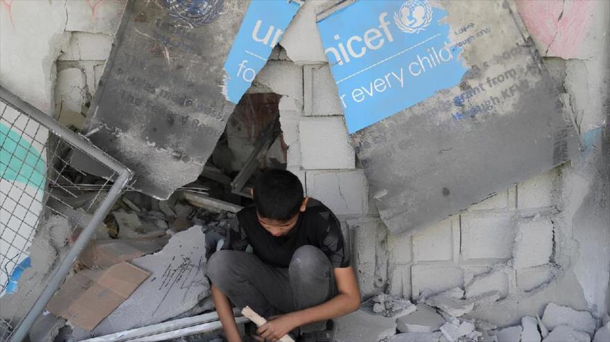 Un niño se sienta bajo un cartel roto de UNICEF mientras palestinos inspeccionan el lugar de un ataque israelí a una escuela que albergaba a personas desplazadas en Ciudad de Gaza. (Foto: Reuters)