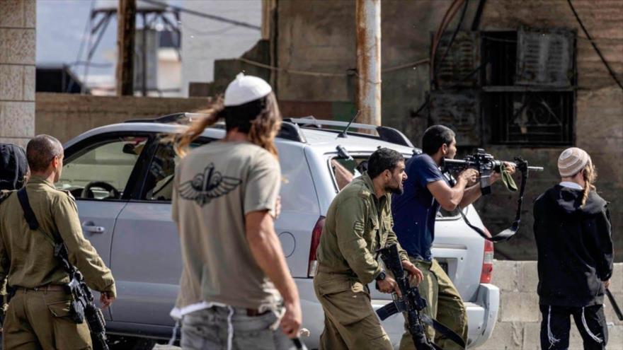 Los colonos israelíes, junto a las fuerzas del ejército sionista, llevan armas en una de las redadas en Cisjordania. 