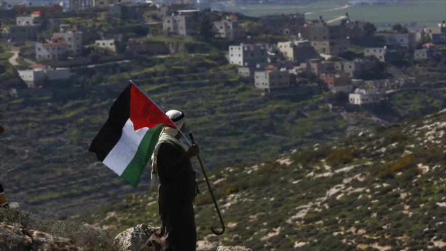 Un palestino ondea la bandera palestina durante una manifestación contra los asentamientos israelíes cerca de Nablus, en Cisjordania, 26 de febrero de 2021. (Foto: EPA)